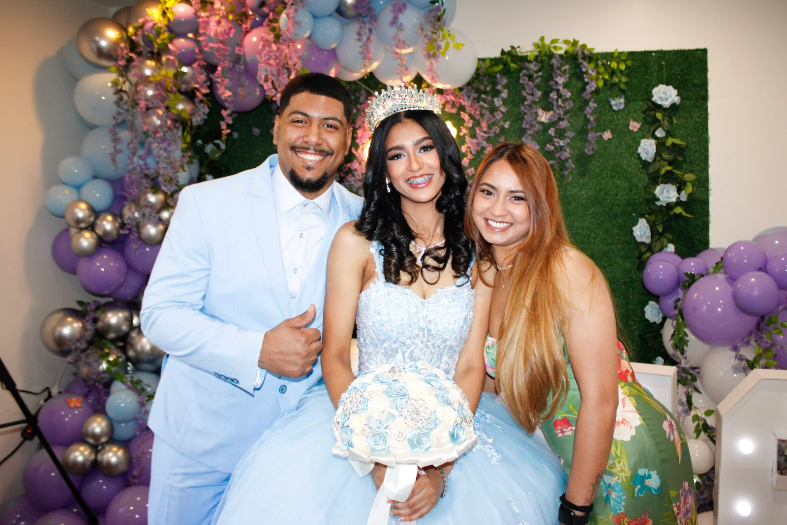 The celebrant holding flowers with two guests in front of pastel balloons