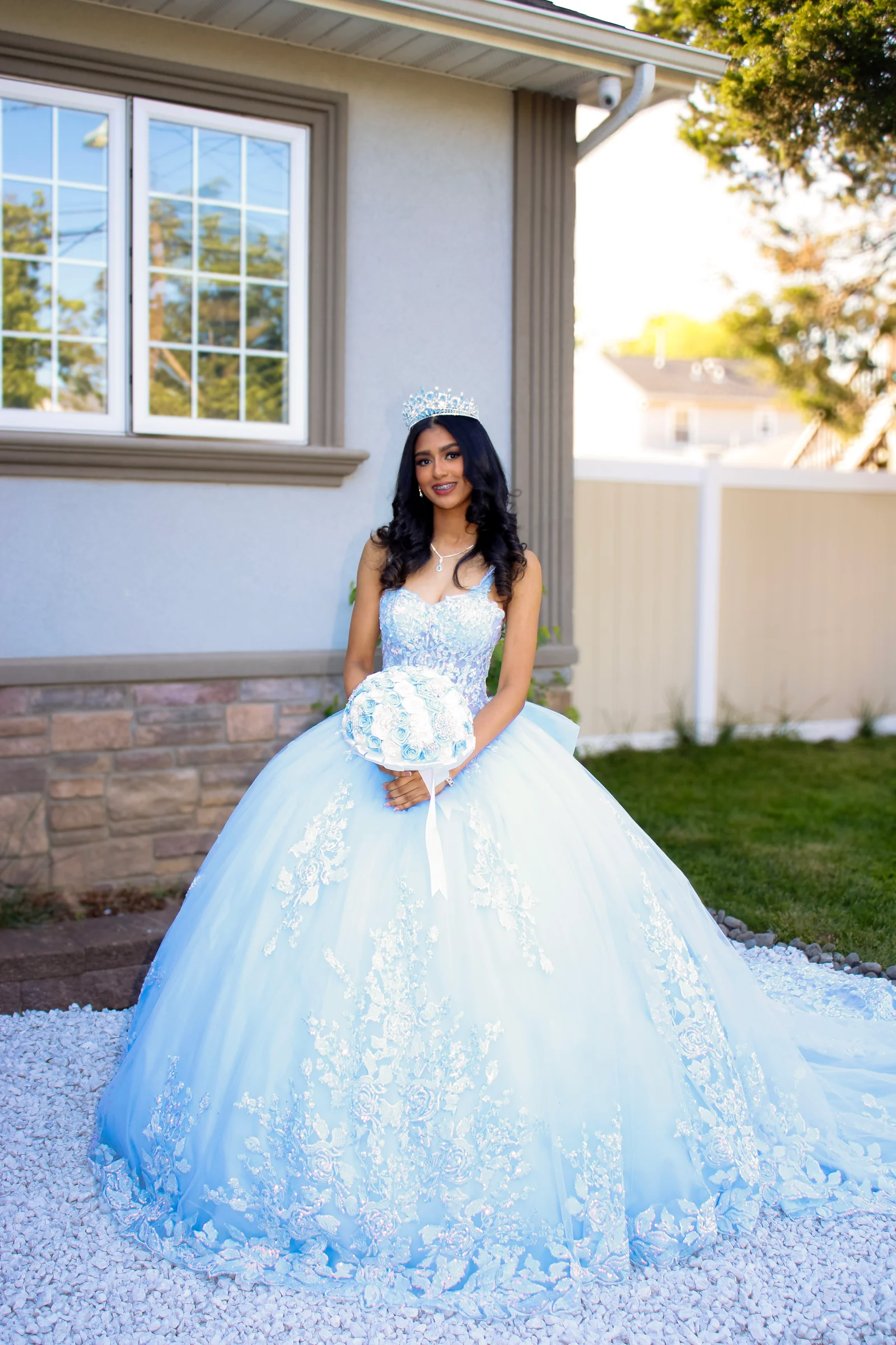 An outdoor portrait of the celebrant holding a bouquet in a pale blue ball gown