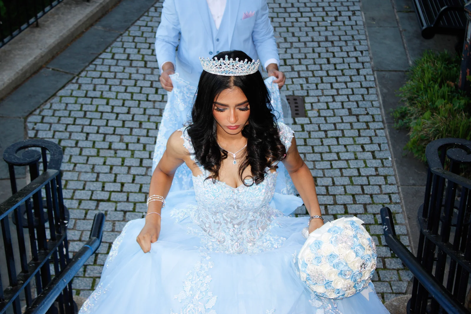 The celebrant descending stone steps in a pale blue ball gown with a bouquet