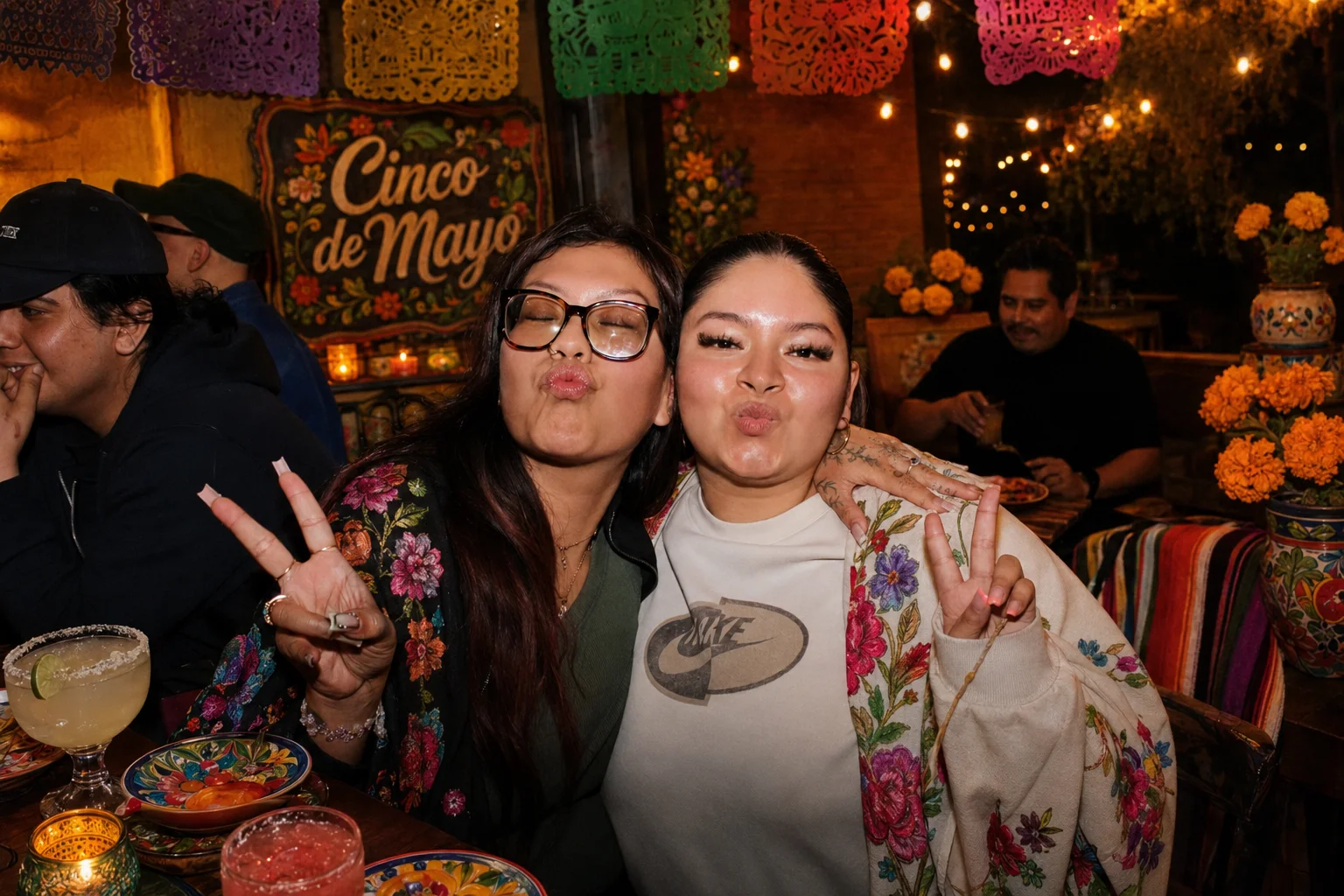 Two guests posing beside orange flowers and Cinco de Mayo decorations at The Ox Tavern at Westwood