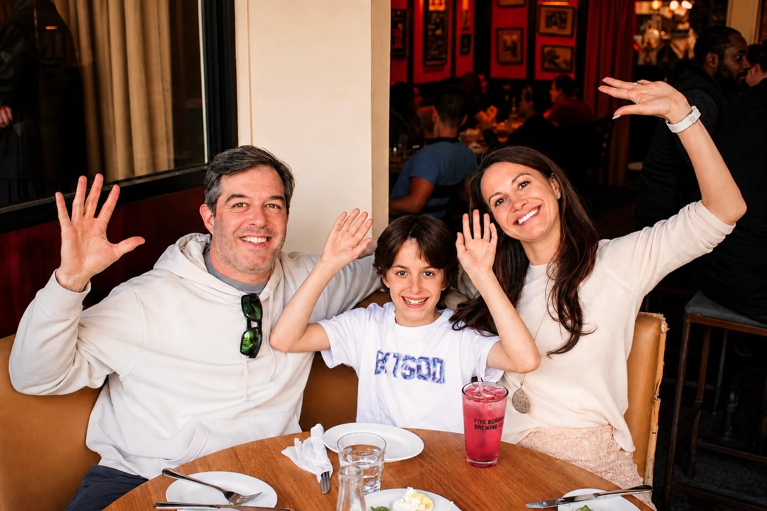 Three guests waving and posing around a restaurant table at The Ox Tavern at Westwood