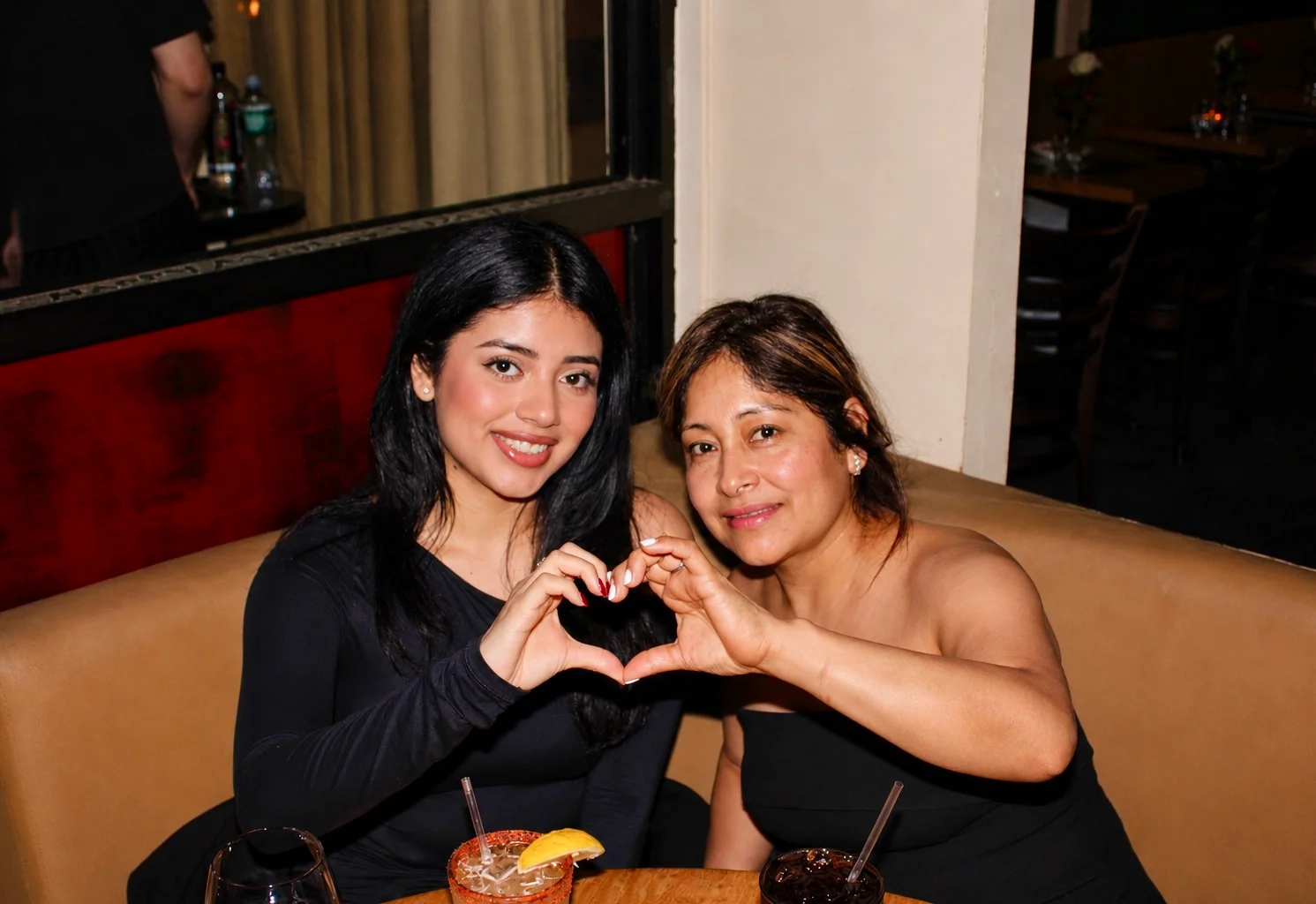Two guests making a heart with their hands in a restaurant booth at The Ox Tavern at Westwood