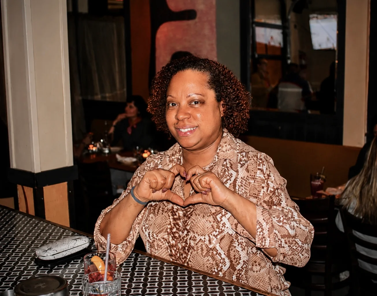 A guest making a heart with her hands beside a candlelit table at The Ox Tavern at Westwood