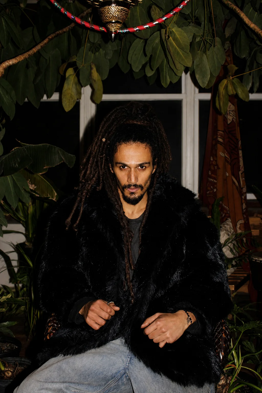 A seated portrait in a dark coat surrounded by green foliage