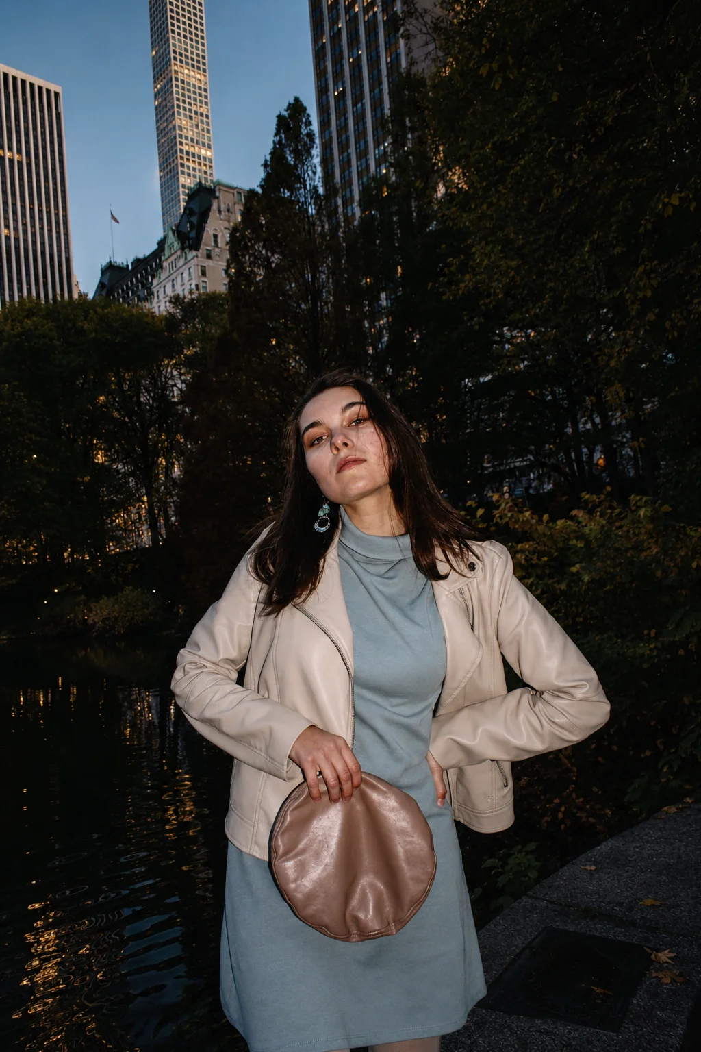 A portrait in a light jacket among trees and city buildings