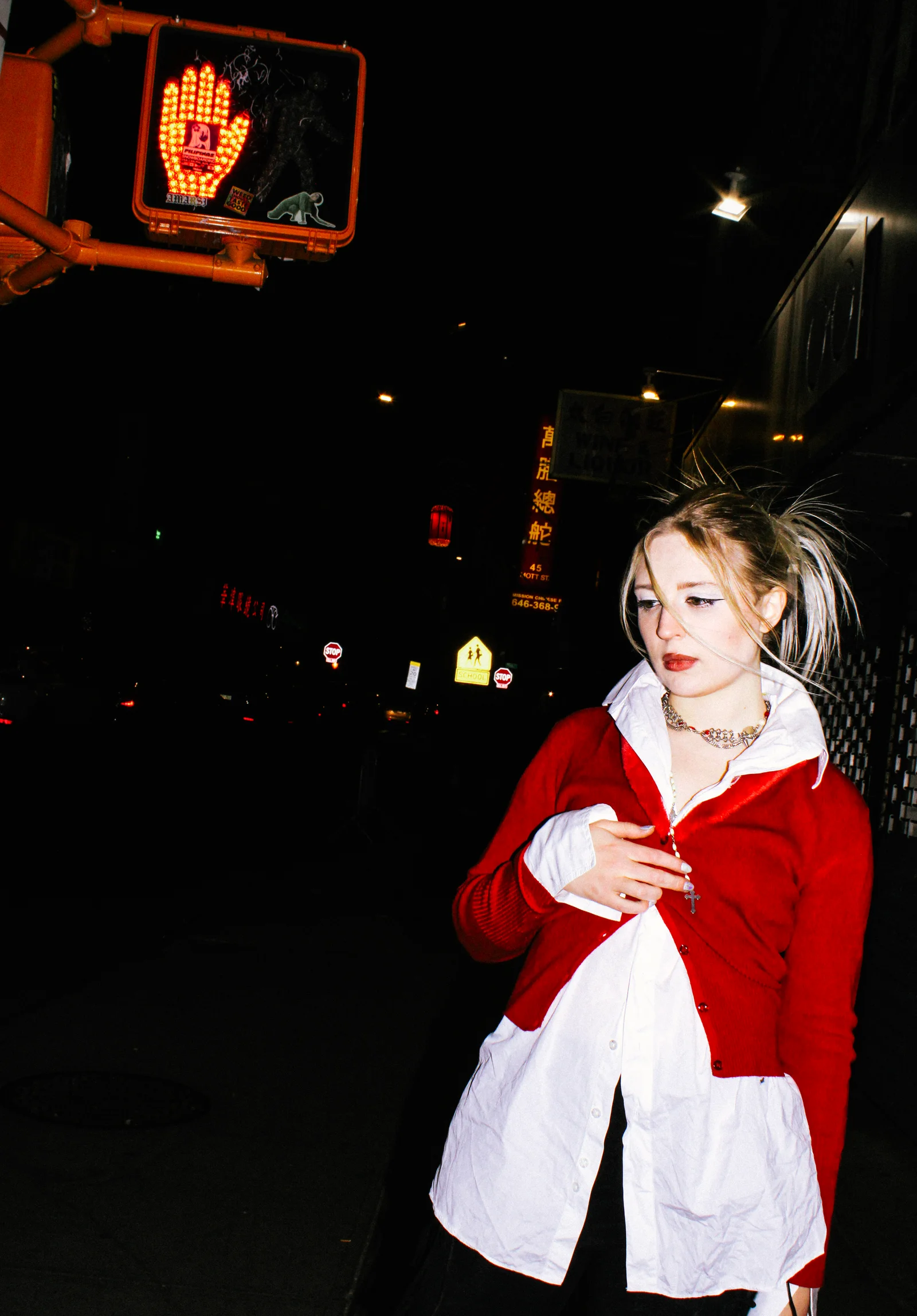A nighttime street portrait in a red cardigan beneath a pedestrian signal