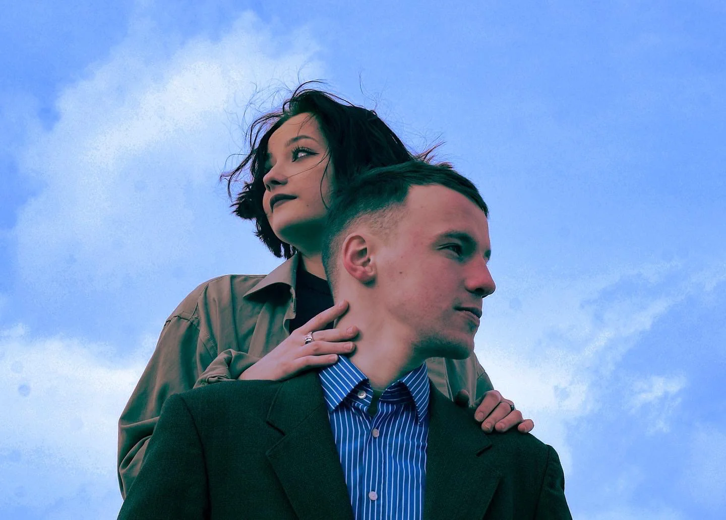 An editorial portrait of two people in tailored jackets beneath a blue sky