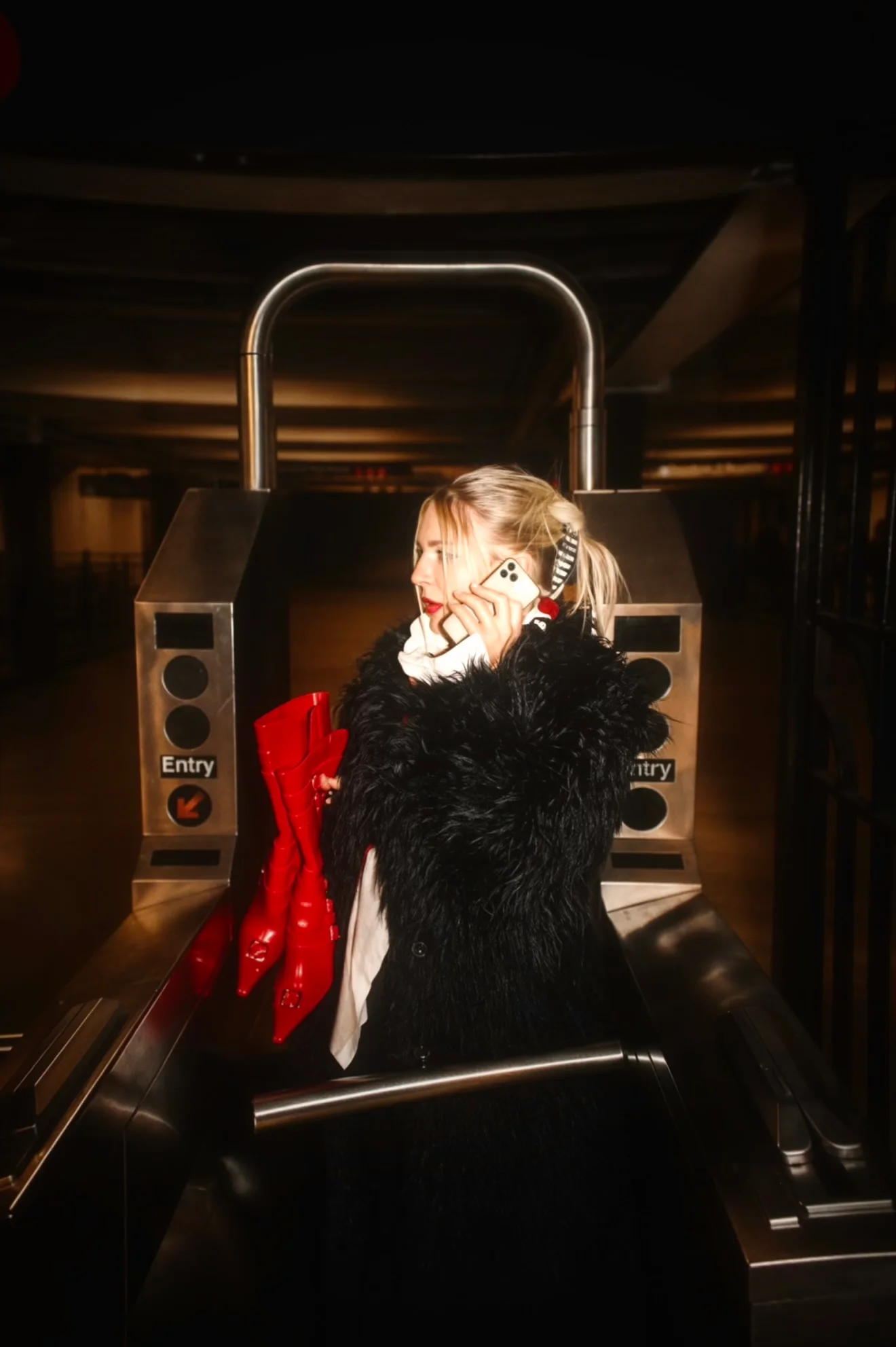 A portrait in a dark coat beside a subway turnstile